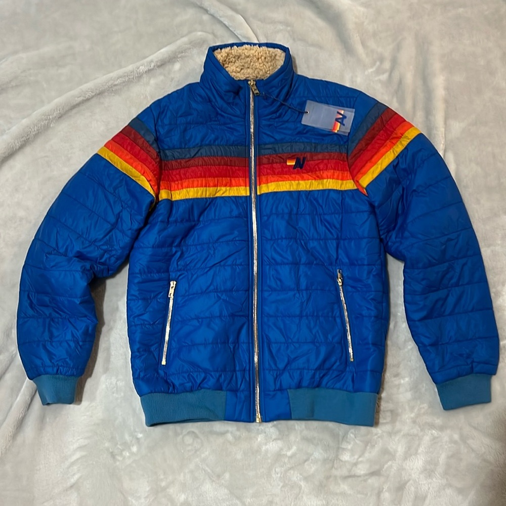 Jacket is Blue with a rainbow going across the chest. It is a Children’s size L.